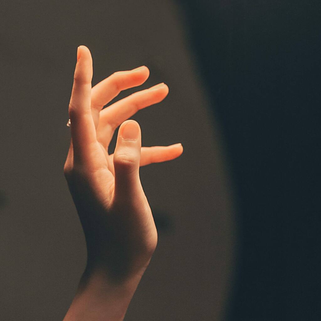 Elegant human hand reaching into soft, warm light creating a serene and artistic effect.